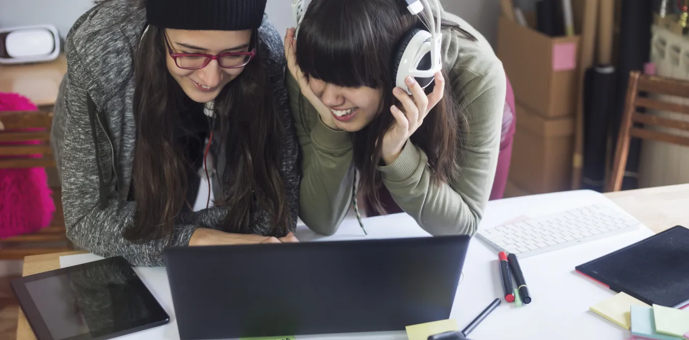 Photo of students using a laptop together with headphones
