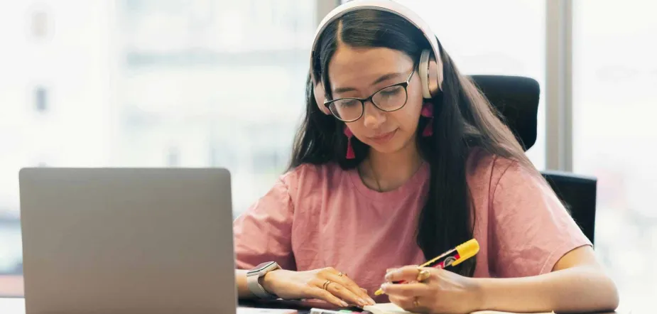 Julia Lopez image of female student studying at a desk with laptop and headphones on