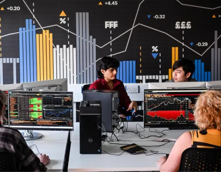 Photo of students at the University of Suffolk's Bloomberg Lab, with charts on screens and graphs on the wall. Image credit: Gregg Brown Photography / University of Suffolk.