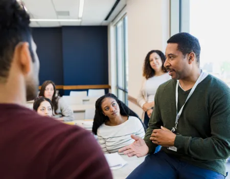 Tutor sits on desk and speaks to group of students