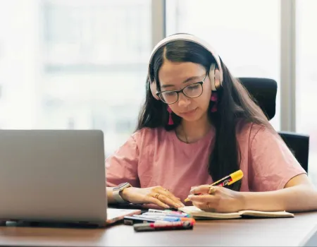 Julia Lopez image of female student studying at a desk with laptop and headphones on