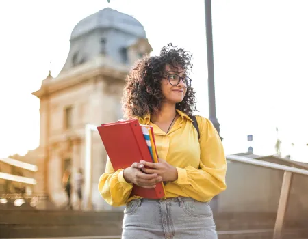 Lady standing outside holding a binder and textbooks