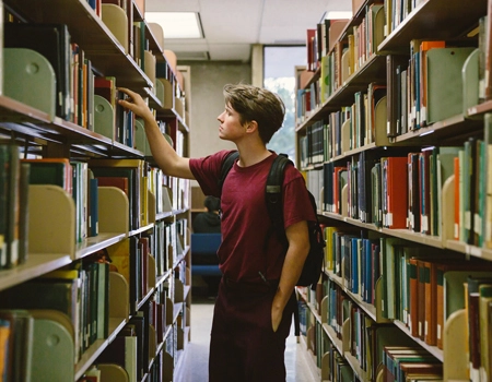 A young man choosing a book from a library shelf